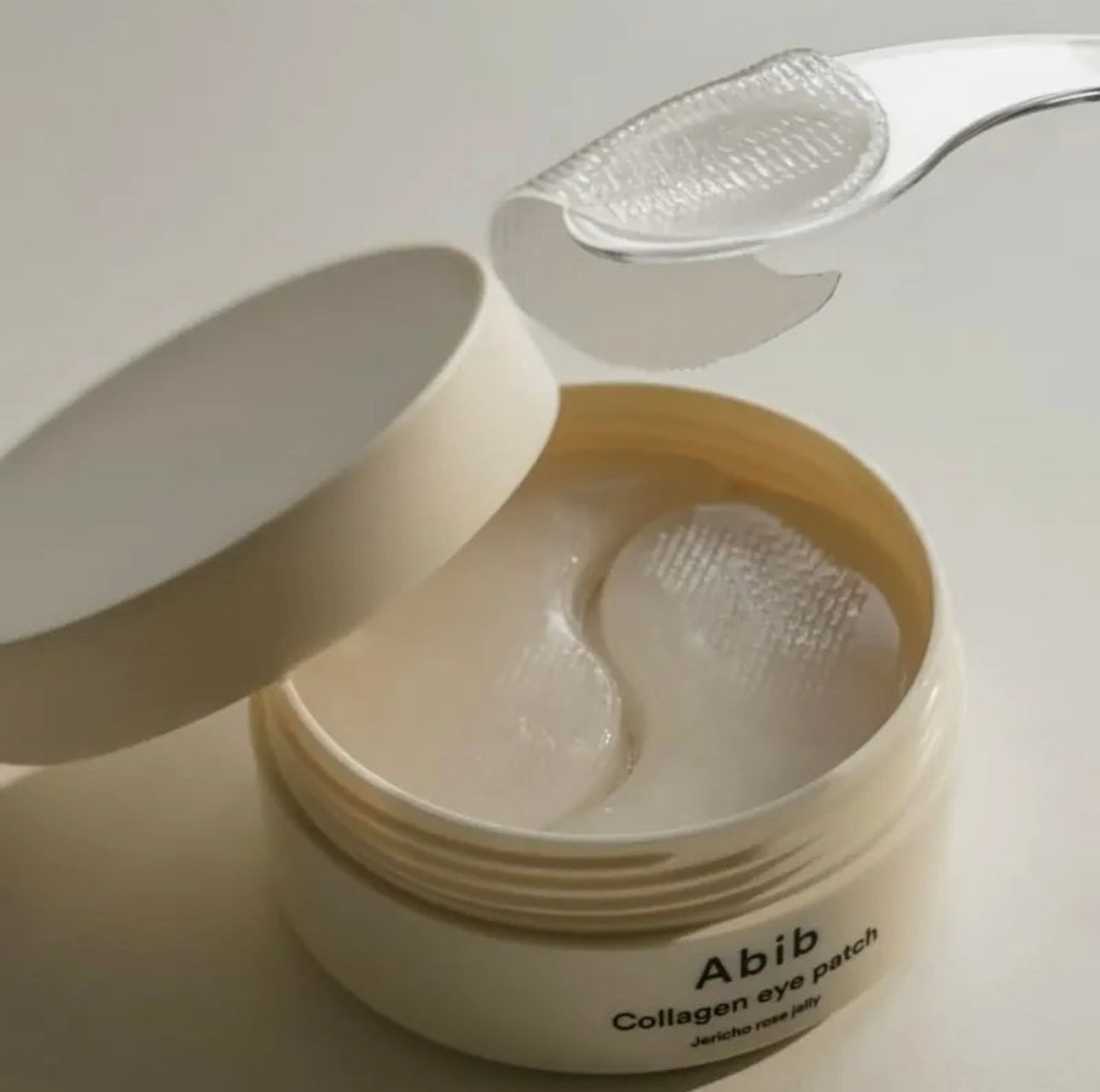 Jar of Abib Collagen eye patches with a spoon on a white background