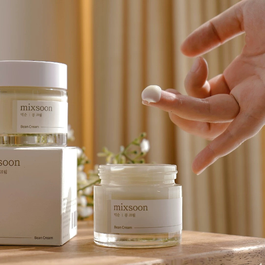 Hand applying cream from a 'mixsoon' jar on a wooden surface with a blurred background