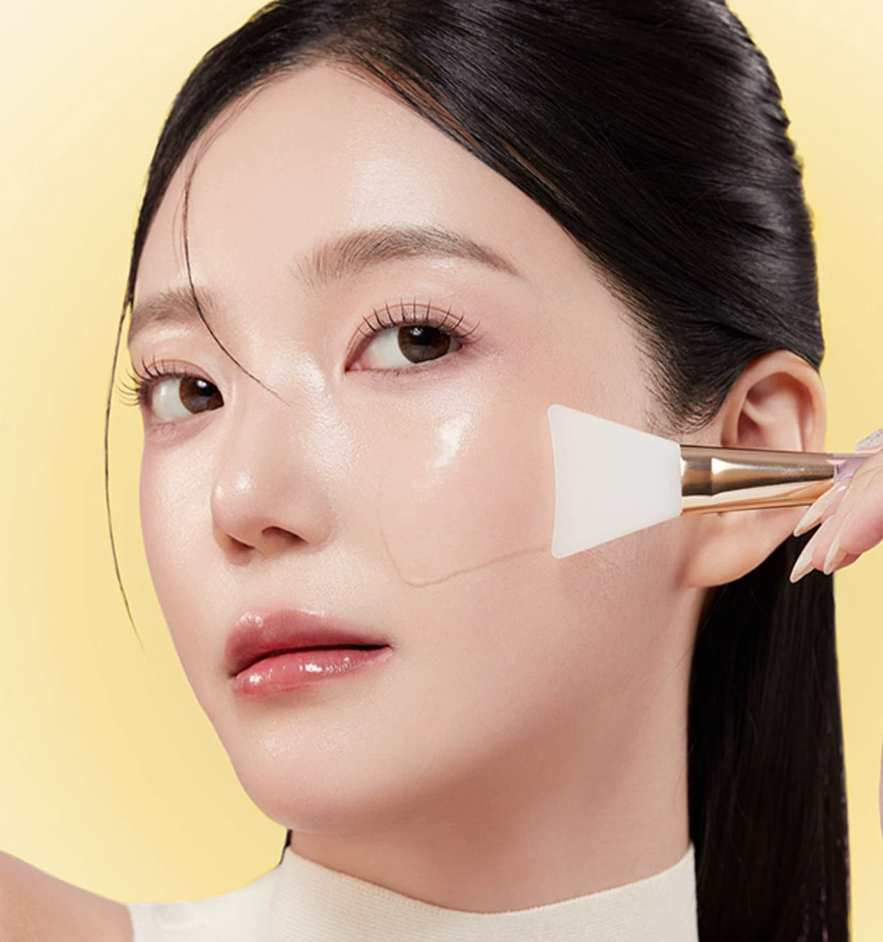 Woman applying a cosmetic product to her face with a brush on a yellow background