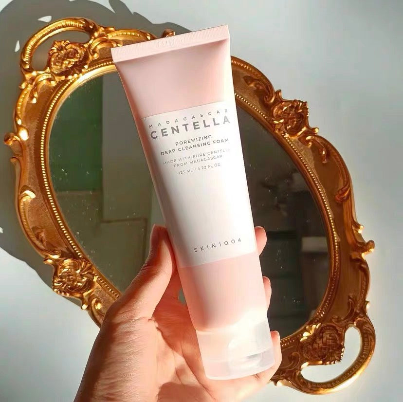 Hand holding a tube of Skinfood Madagascan Centella cleansing foam in front of an ornate mirror.