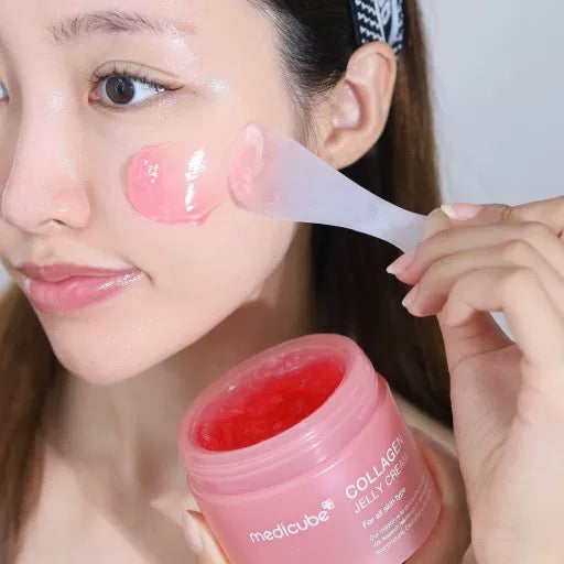 Woman applying pink jelly cream to her face with a applicator, next to a jar of Medicube Collagen Jelly Cream.